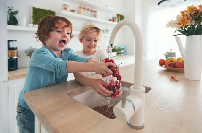 Freudige Kinder waschen Kirschen unter fließendem Wasser